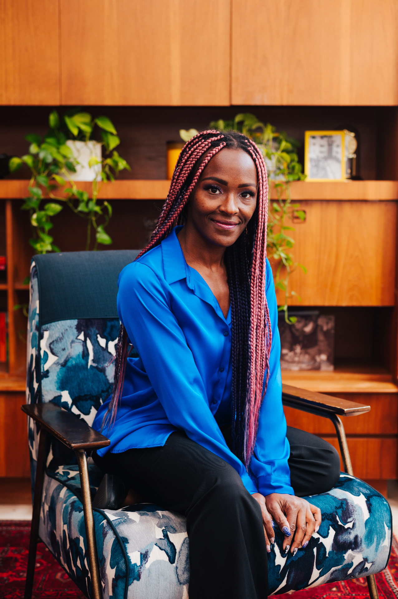 Kerry McKenzie, Canadian entrepreneur and facilitator, smiling, seated in a patterned armchair against a warm wood backdrop.